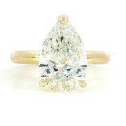 A close-up photo of a gold ring with a rectangular, clear gemstone set in the center, displayed on a white background. The ring features a simple, elegant band and a modern, minimalist design.
