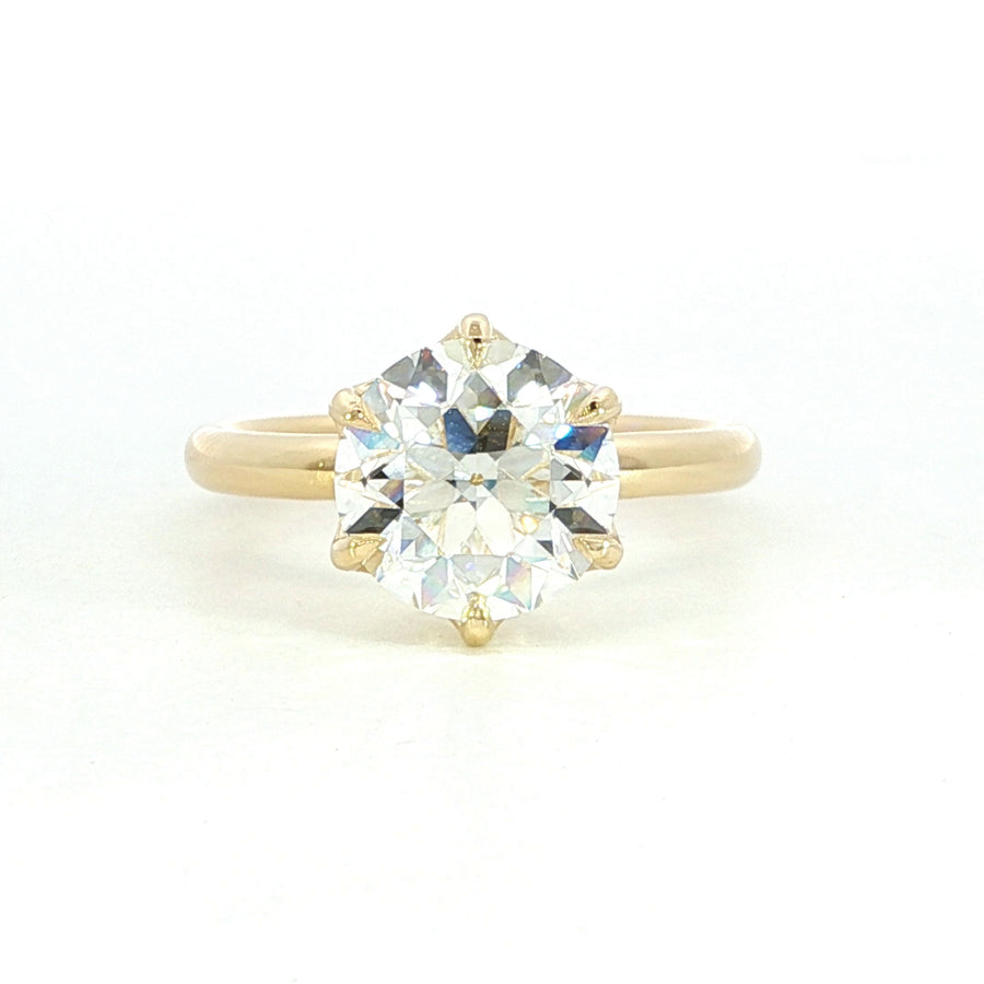 A close-up photo of a gold ring with a rectangular, clear gemstone set in the center, displayed on a white background.