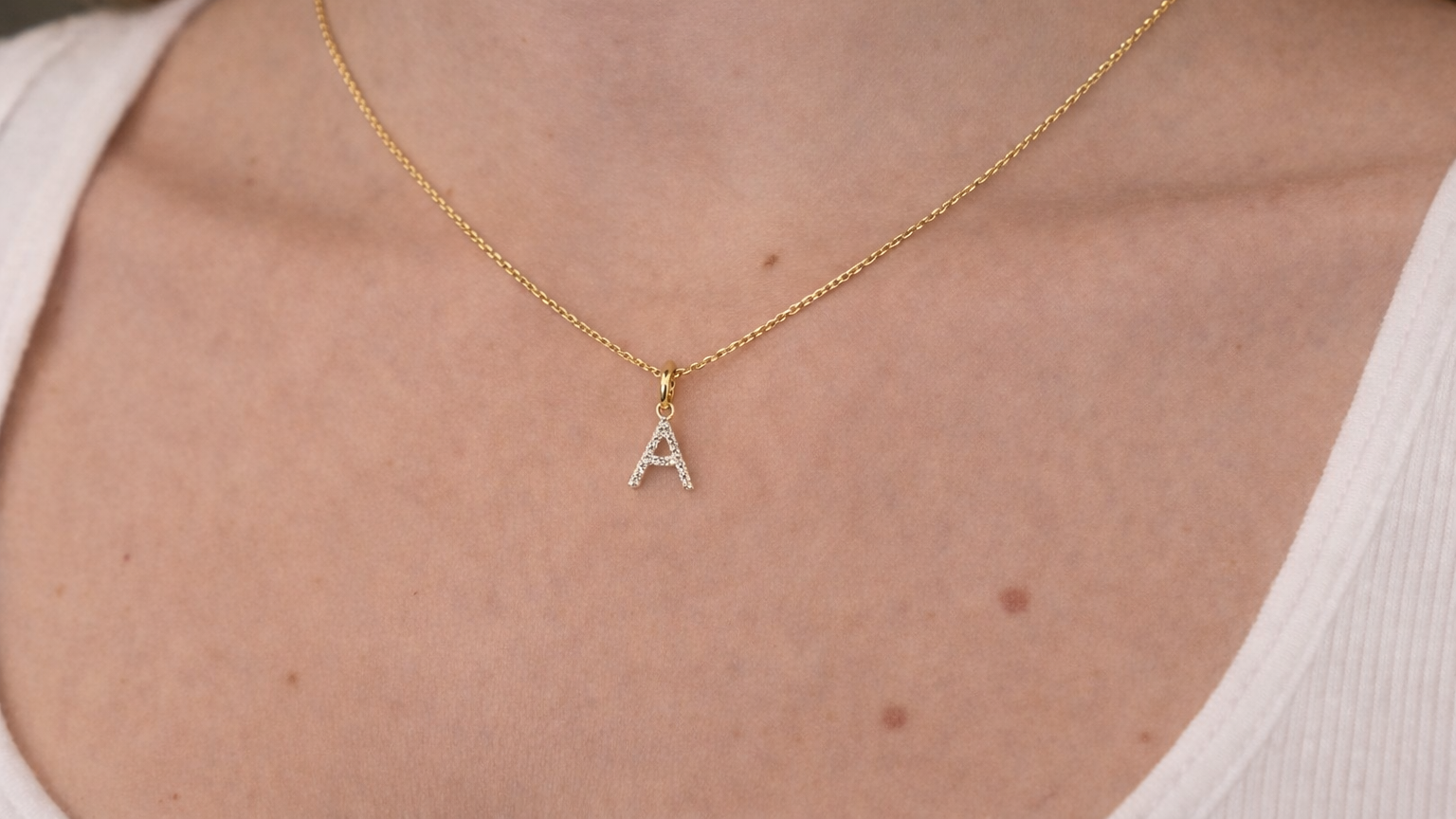 Gold necklace with a diamond 'A' pendant on a person wearing a white top.