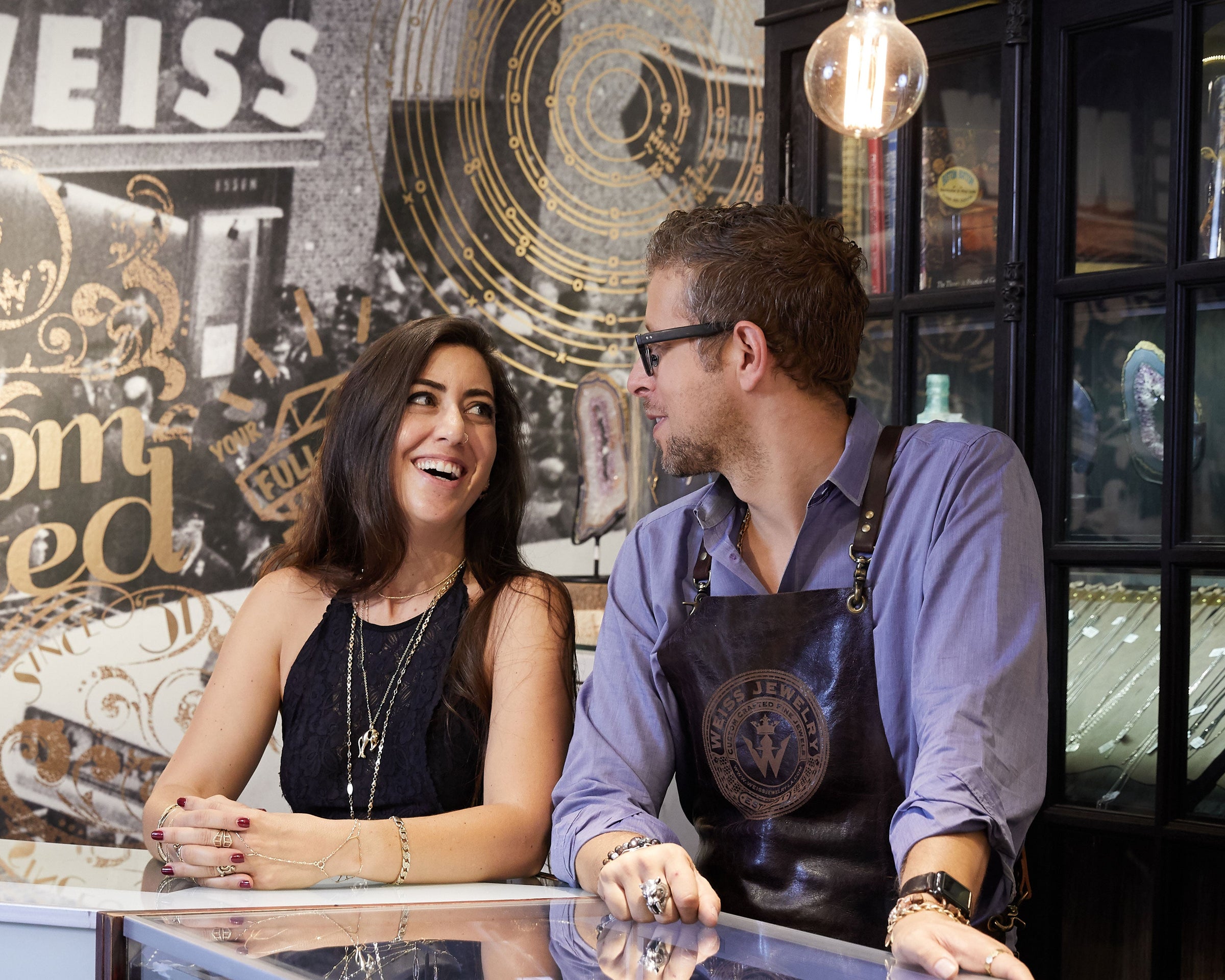 Man and woman in a jewelry store with a display case and decorative wall.
