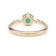 A 14K solid yellow gold ring featuring a vivid green emerald centerpiece, photographed from the back to showcase its smooth, polished band and secure gemstone setting.