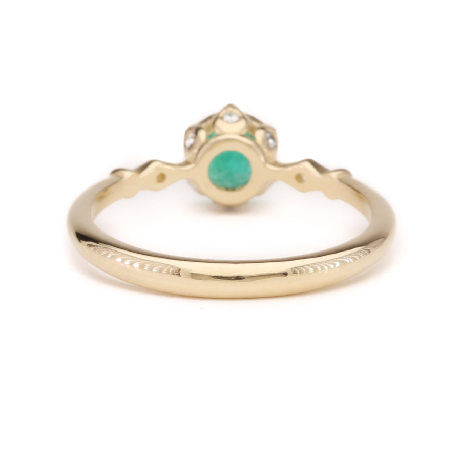 A 14K solid yellow gold ring featuring a vivid green emerald centerpiece, photographed from the back to showcase its smooth, polished band and secure gemstone setting.