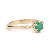 A delicate 14K solid yellow gold ring featuring a vibrant green emerald centerpiece in a fairytale-inspired setting, photographed from the side to showcase its elegant band and intricate design details.