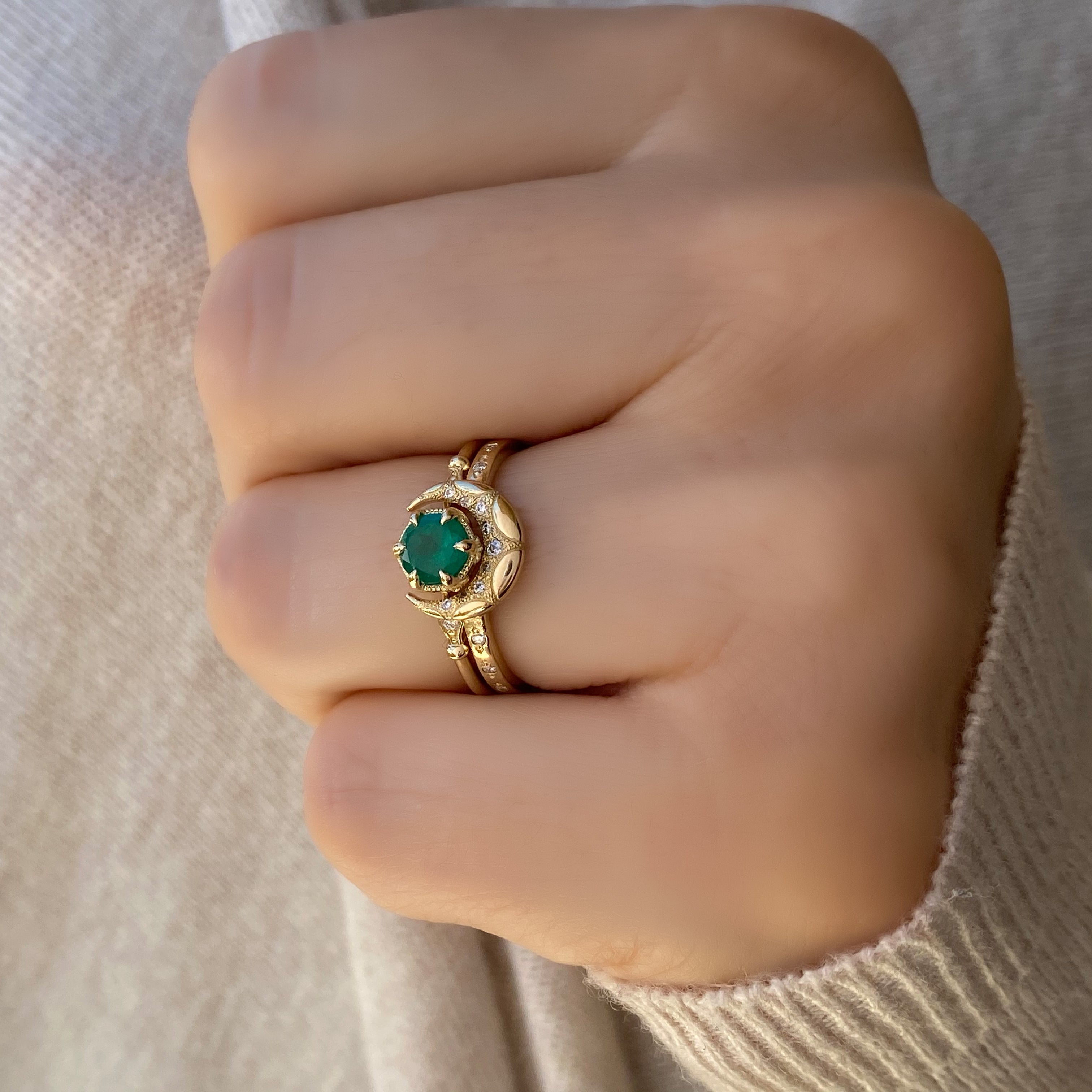 A close-up image of two elegant 14kt solid gold rings: one features a round emerald gemstone in a classic setting, and the other is a crescent horn-shaped band. Both rings are displayed side by side on a neutral background, highlighting their fine craftsmanship and vibrant green gemstone.