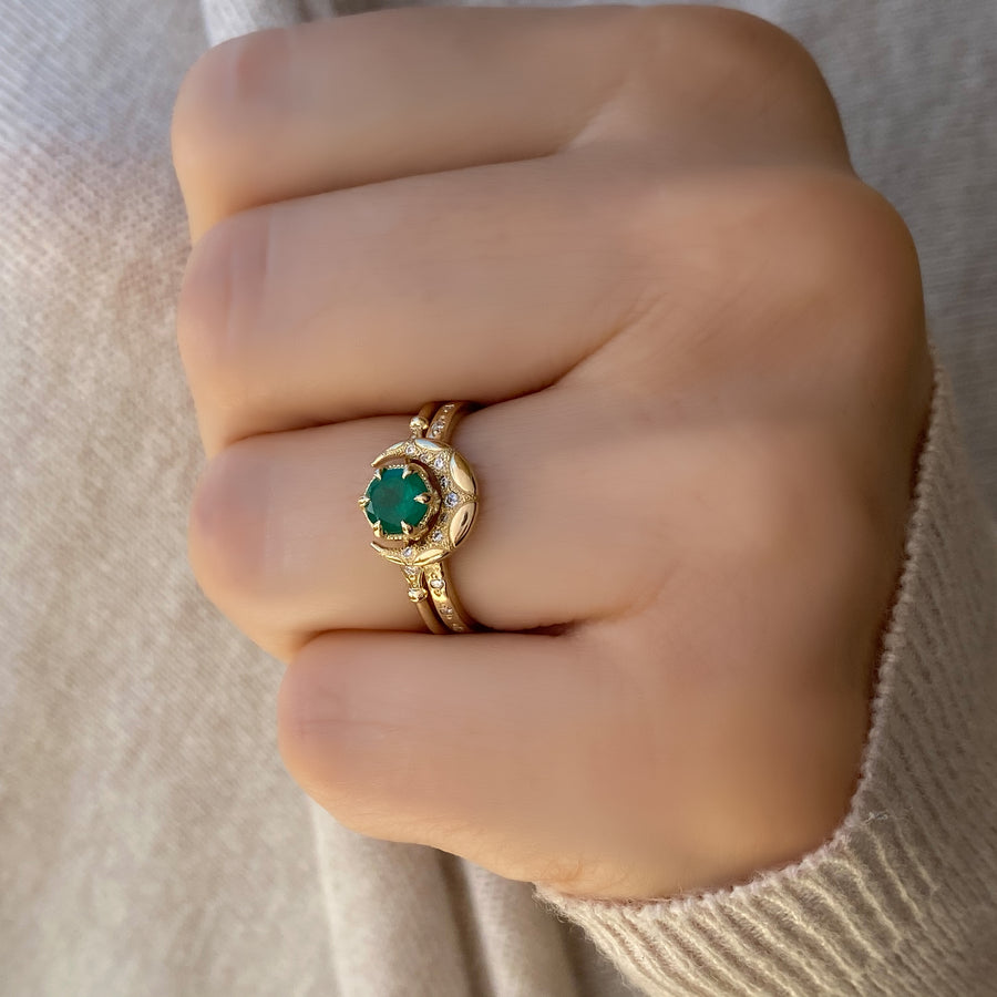 A close-up image of two elegant 14kt solid gold rings: one features a round emerald gemstone in a classic setting, and the other is a crescent horn-shaped band. Both rings are displayed side by side on a neutral background, highlighting their fine craftsmanship and vibrant green gemstone.